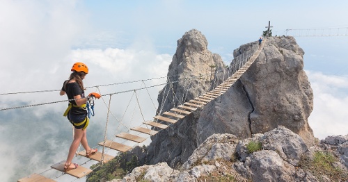 Woman crossing chasm on narrow bridge.